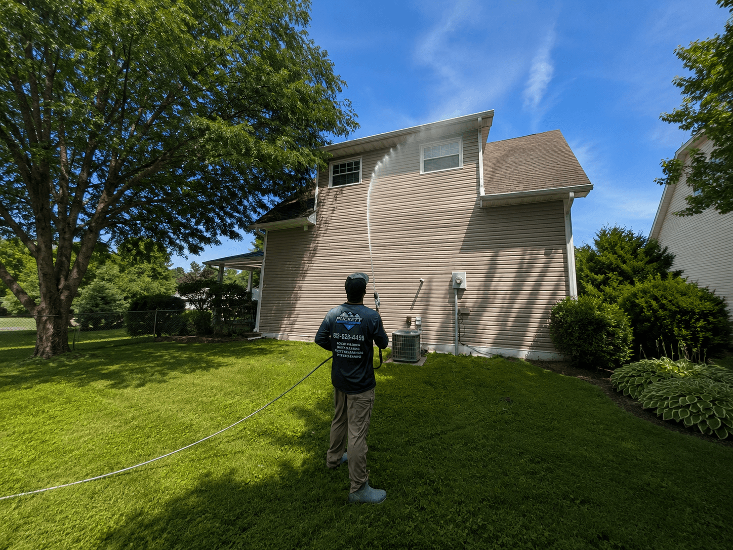 A Puckett Exteriors technician soft washing the siding of a two-story home